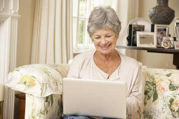 Retired Senior Woman Sitting On Sofa At Home Using Laptop