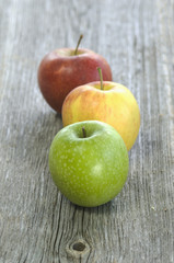 Grüner, gelber und roter Apfel in einer Reihe auf Holz