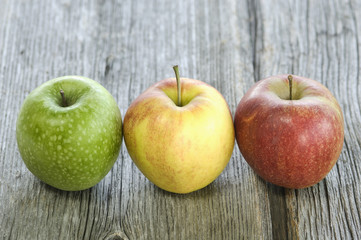 Grüner, gelber und roter Apfel in einer Reihe auf Holz