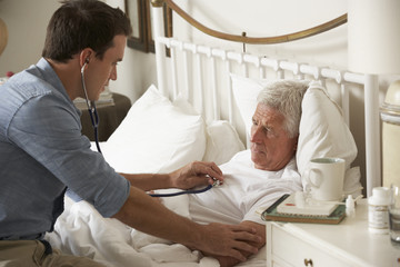 Fototapeta premium Doctor Examining Senior Male Patient In Bed At Home