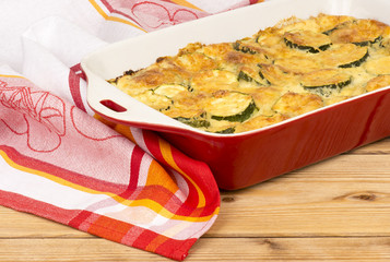 Casserole with cheese and zucchini in baking dish on the wooden background.