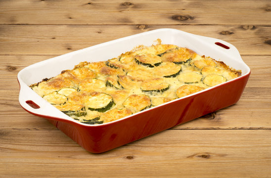 Casserole with cheese and zucchini in baking dish on the wooden background.