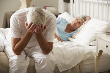 Worried Senior Man Sits On Bed Whilst Wife Sleeps - obrazy, fototapety, plakaty