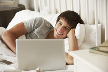 Teenage Boy Using Laptop In Bed At Home