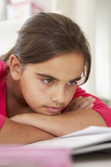 Naklejka premium Bored Young Girl Doing Homework At Desk In Bedroom