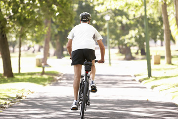 Rear View Of Mature Man Cycling Through Park
