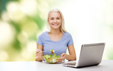 smiling woman eating salad with laptop