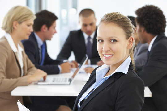 Portrait Of Female Executive With Office Meeting In Background