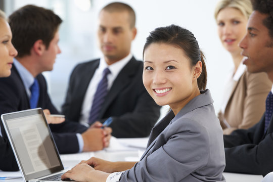 Portrait Of Female Executive With Office Meeting In Background