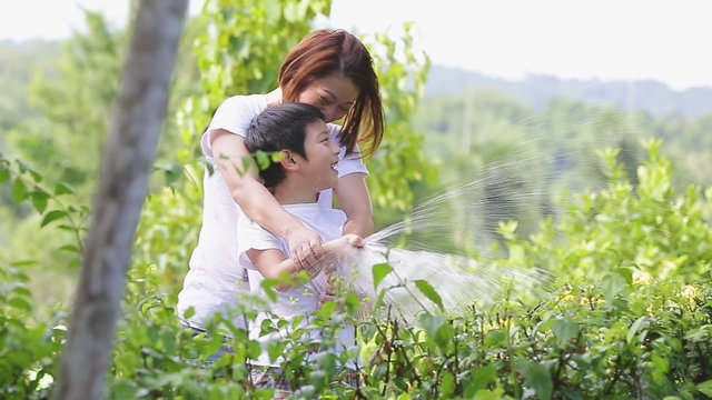 Asian mother and son are watering the tree, standing in the shade of a tree in the garden