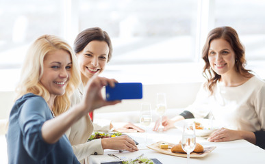 Fototapeta premium women with smartphone taking selfie at restaurant