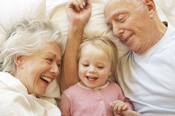 Grandparents Cuddling Granddaughter In Bed - obrazy, fototapety, plakaty