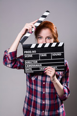 Beautiful red-haired woman holding a movie clapper.