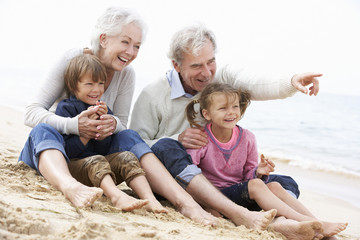 Grandparents And Grandchildren Sitting On Beach Together - obrazy, fototapety, plakaty