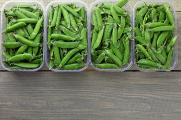 fresh green peas in a plastic container on a wooden background