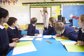Pupils Sitting At Table As Teacher Stands By Whiteboard