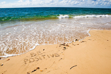 Fototapeta na wymiar Be positive. Creative motivation concept written in the sand at the beach.