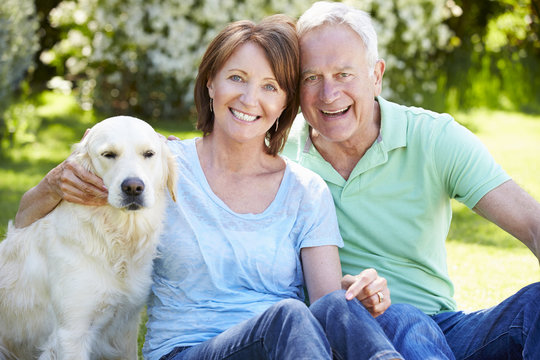 Portrait Of Senior Couple Sitting In Garden With Dog