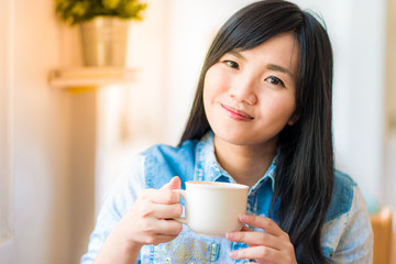 Happy asian young woman sitting in vintage cafe with cup of coff