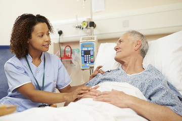 Nurse Sitting By Male Patient's Bed In Hospital