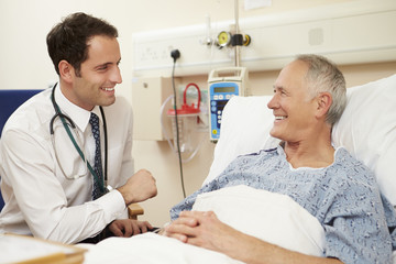 Doctor Sitting By Male Patient's Bed In Hospital