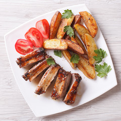 Grilled ribs, potatoes and tomatoes on a plate closeup. top view
