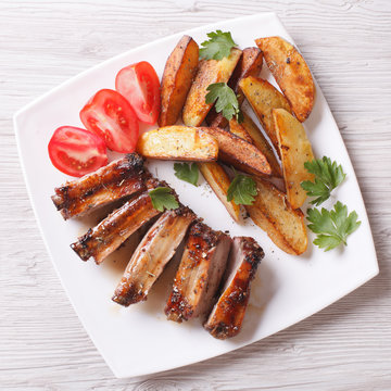 Grilled ribs, potatoes and tomatoes on a plate closeup. top view
