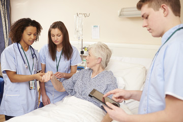 Trainee Nursing Staff By Female Patient's Bed In Hospital