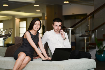 two business people man and woman working on a computer while waiting in airport lounge