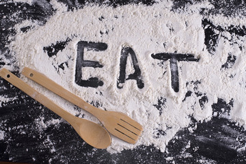 Word eat written in flour with a wooden spoon and fork