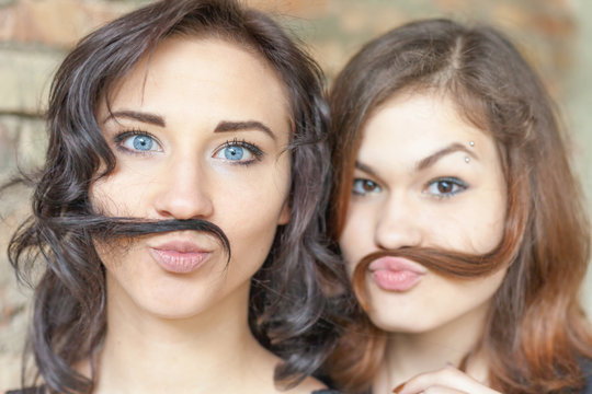 Two young pretty girls making mustache of their hair