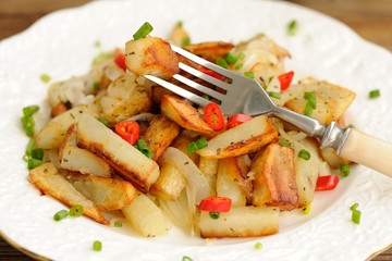 Fried potatoes with scallion and chili in white plate with fork