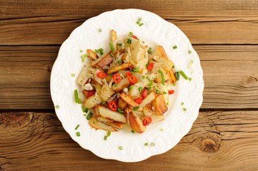 Fried potatoes with scallion and chili in white plate on wooden
