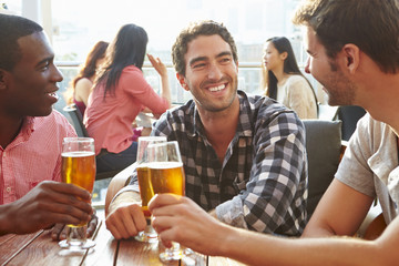 Three Male Friends Enjoying Drink At Outdoor Rooftop Bar