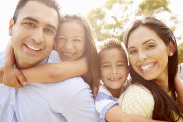 Parents Giving Children Piggyback Ride In Garden