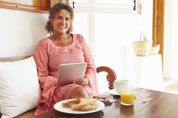 Mature Woman Sitting At Breakfast Table Using Digital Tablet