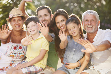 Multi Generation Family Sitting In Garden And Waving