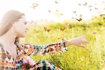  Girl sitting in a meadow in a swarm of flitting butterflies.