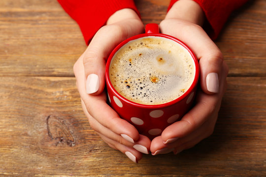 Female hands holding cup of coffee on wooden background