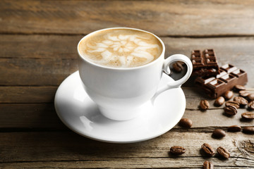 Cup of coffee latte art with grains and chocolate on wooden background