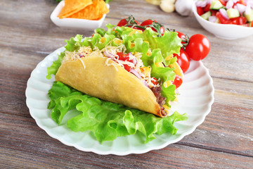 Tasty taco with vegetables on plate on table close up