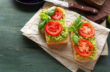 Vegan sandwich with avocado and vegetables on cutting board, on wooden background