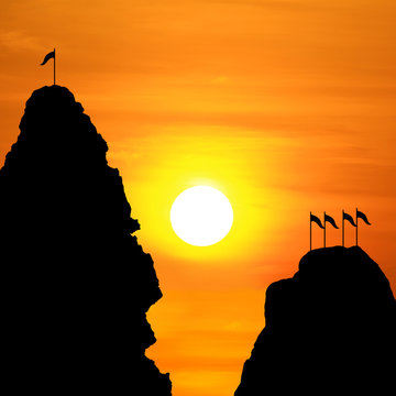 Silhouette against the backdrop of the cliff mountains and flag on the peak in an evening sunsets.