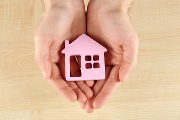 Female hands holding house on wooden background