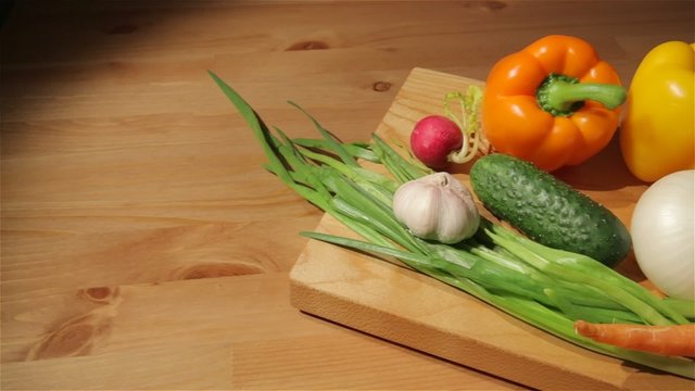 Sliding view of cucumbers, radish, onion, tomatoes and garlic on a cutting board