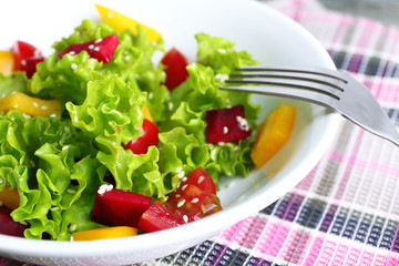 Bowl of fresh green salad on table with napkin, closeup