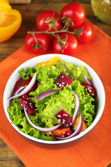 Bowl of fresh green salad on table with napkin, closeup