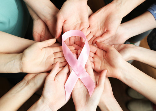 Group of female hands with pink ribbon as breast cancer awareness symbol, closeup