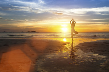 Woman standing at yoga pose on the beach during amazing sunset.