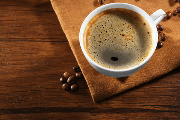 Cup of fresh coffee with beans on table, closeup